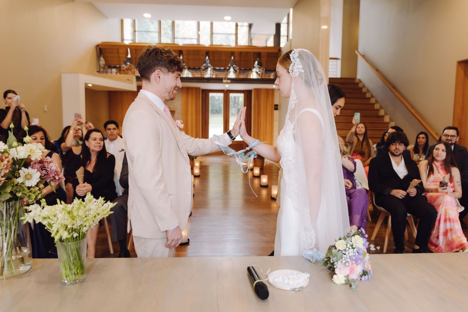 Groom reads vows to veiled bride during wedding ceremony with guests watching.
