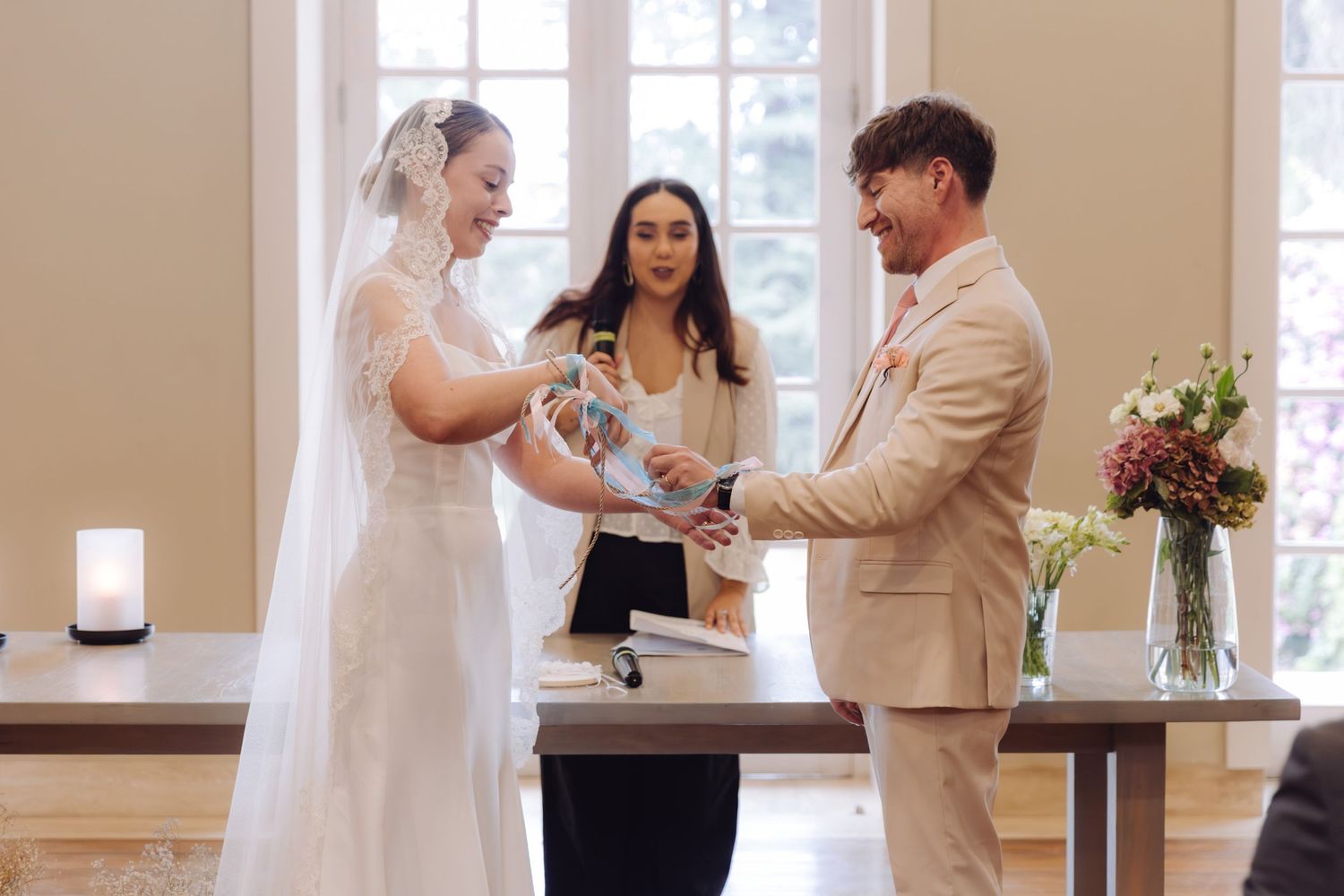 Bride and groom exchange wedding rings with smiling officiant during ceremony.