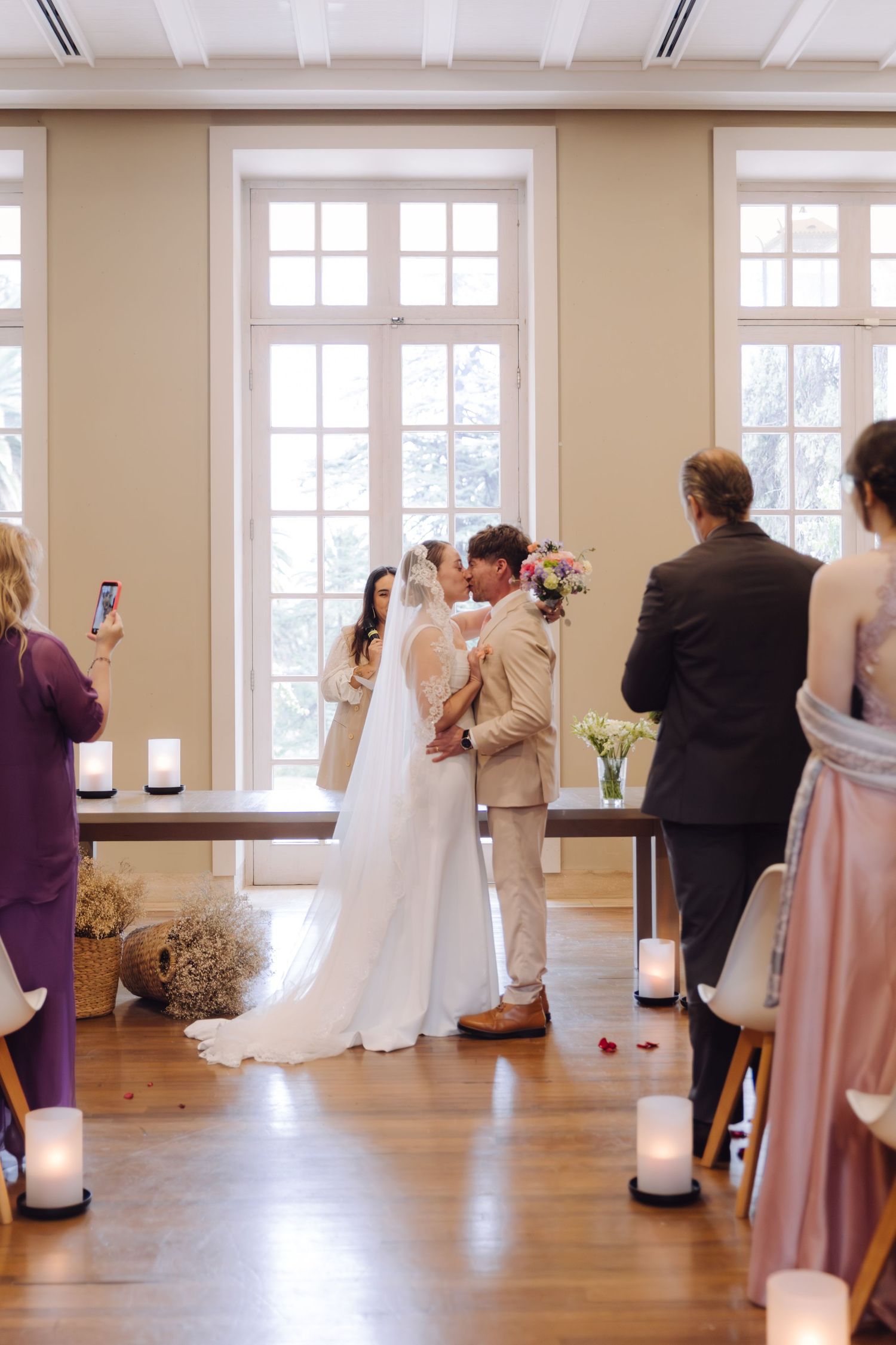 Bride and groom share first kiss during candlelit indoor wedding ceremony.