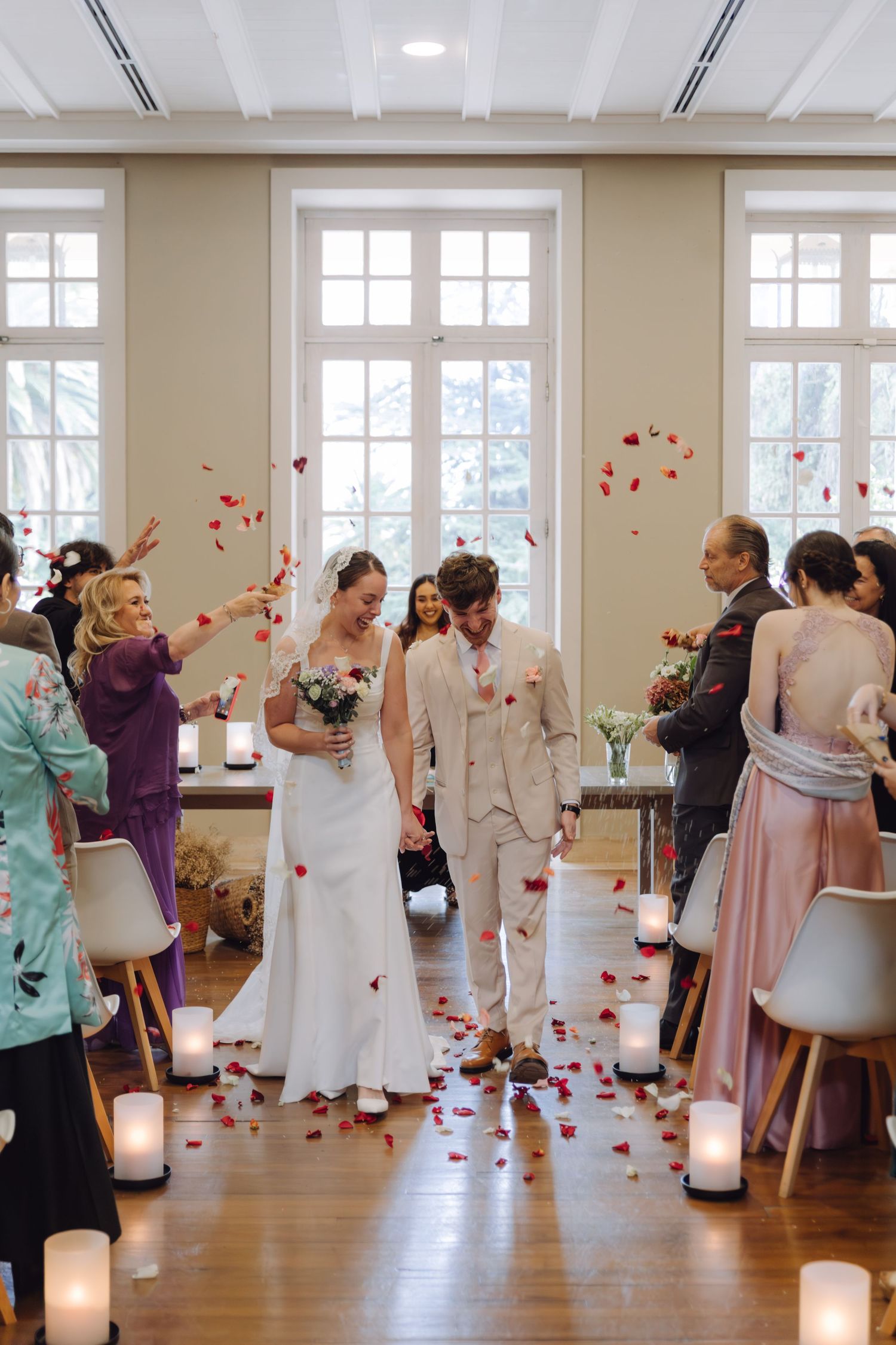 Happy couple walks through rose petal shower during indoor wedding ceremony recessional with candles.