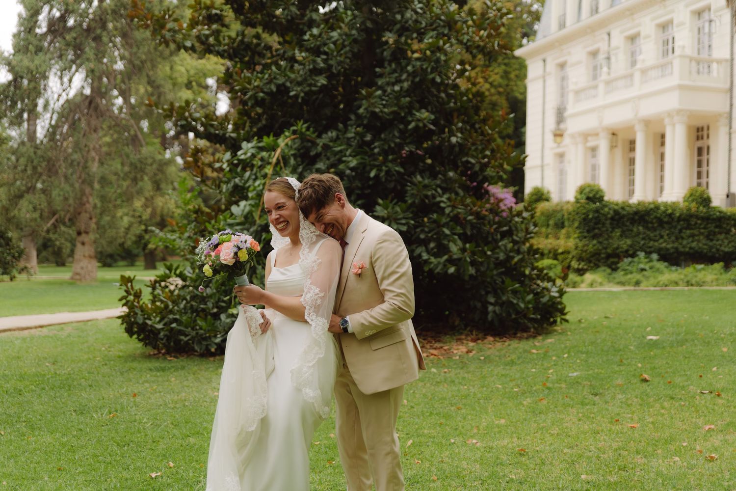 Bride and groom share a tender moment on a lush lawn beside an elegant mansion.