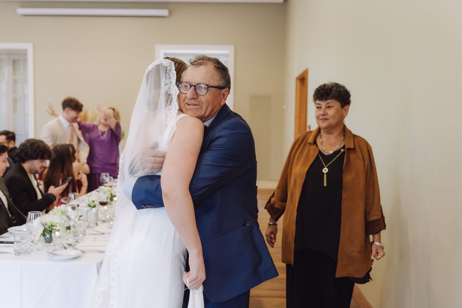 Father of the bride shares a warm embrace with his daughter in a wedding veil at the reception.