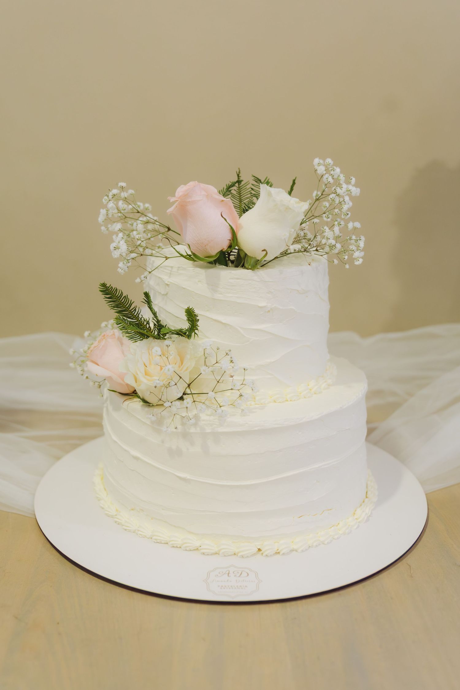 Elegant two-tier white wedding cake decorated with pink roses and baby's breath on a white stand.