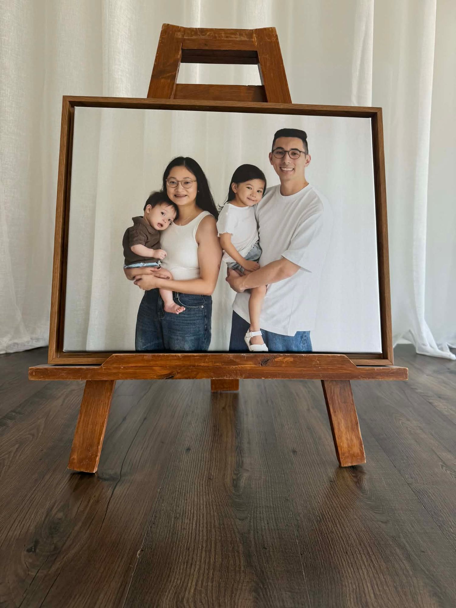 Framed family portrait photo on wooden easel showing parents holding two young children against white background.