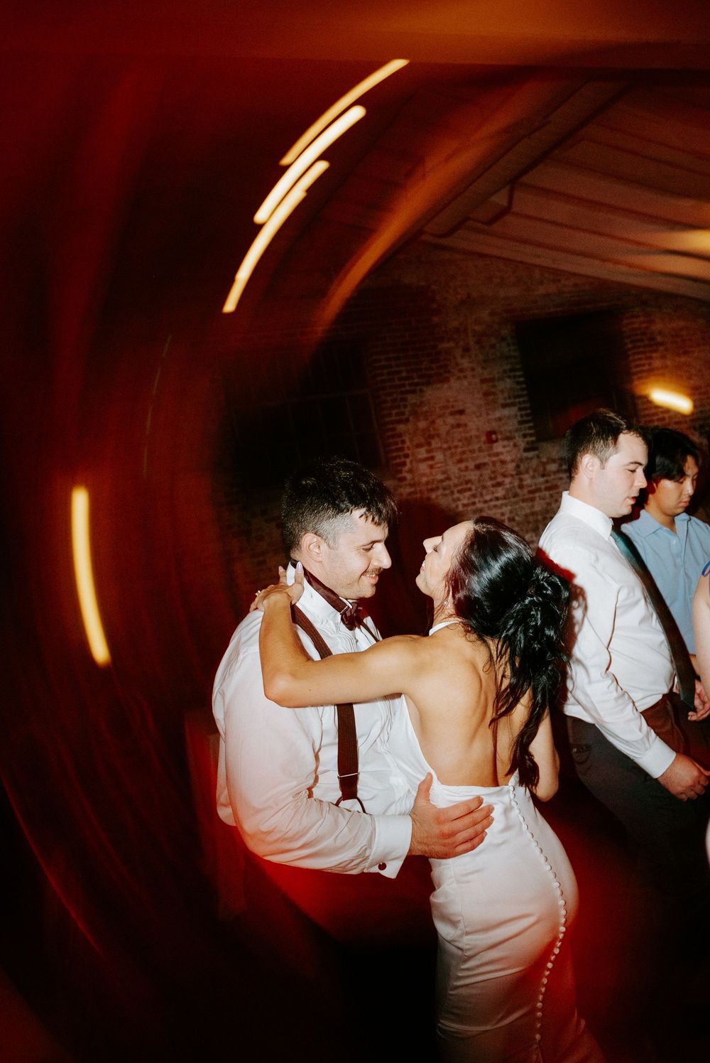 Couple shares romantic first dance at wedding reception in brick venue with warm red lighting.
