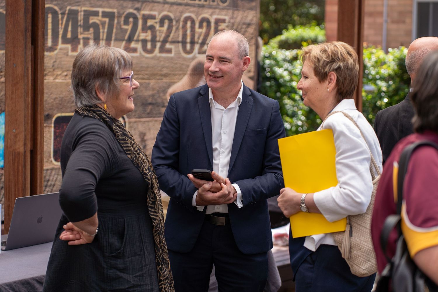 Three professionals networking and conversing at an outdoor business event or conference.