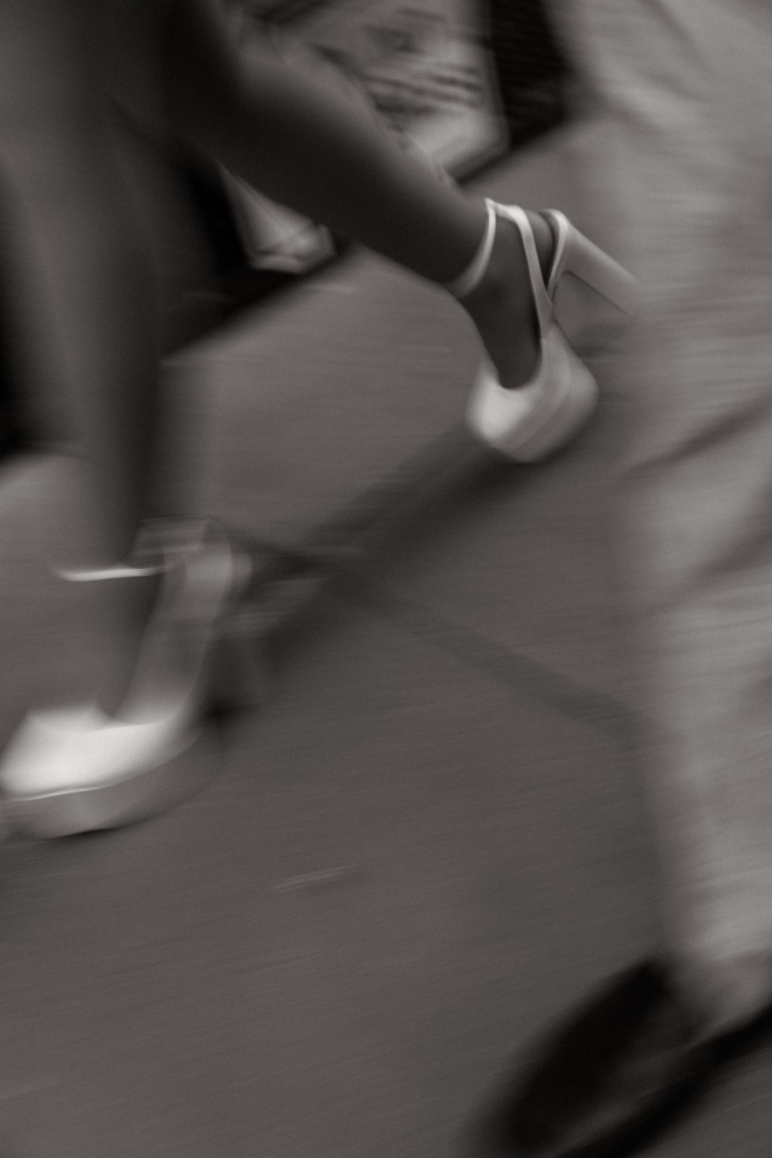 Blurred black and white photo of people walking, capturing motion of feet in heels on pavement.