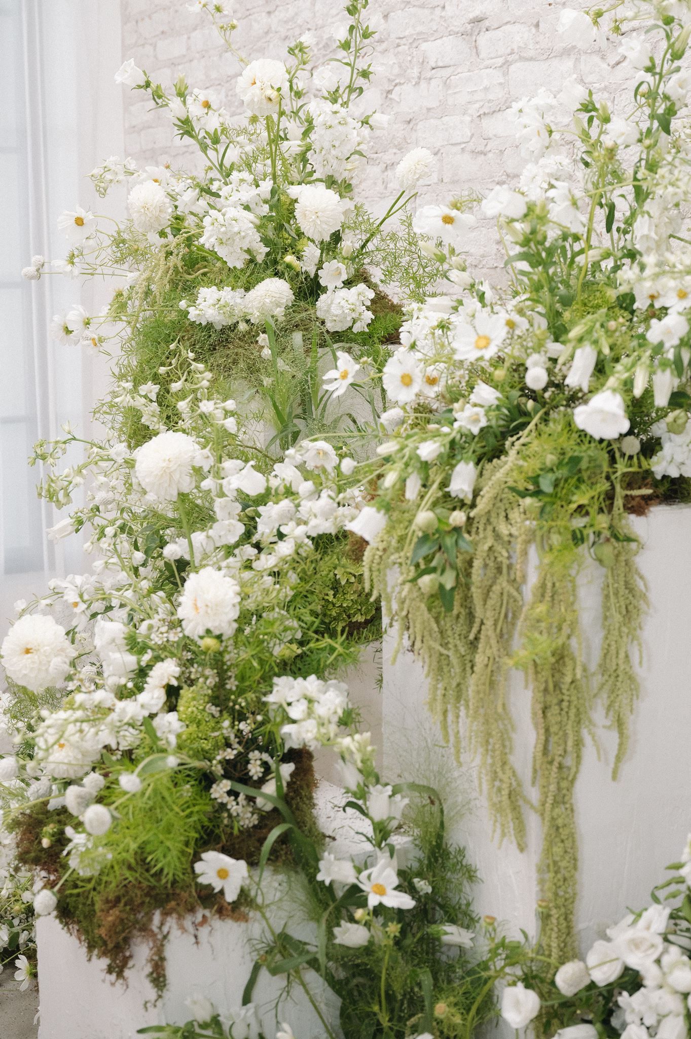 Lush white floral arrangement with green foliage cascading down white pillars at Oak Atelier in Conroe, Texas.