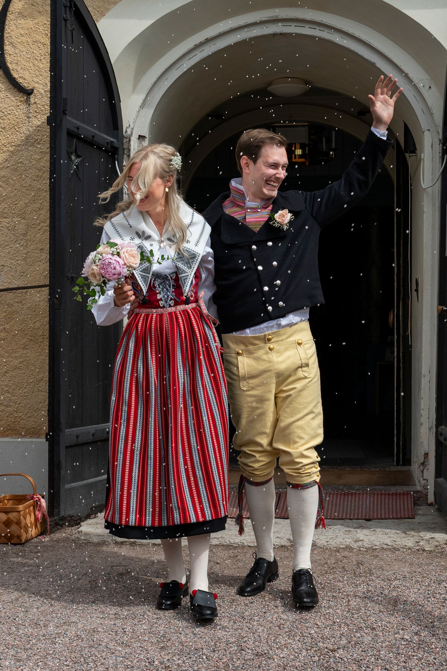Couple in traditional Scandinavian folk costumes celebrating wedding exit with confetti, bride holding bouquet.