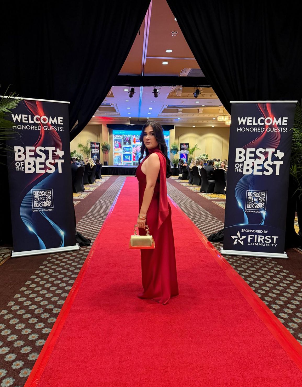 Woman in red gown on red carpet at Best of the Best awards event with welcome banners.