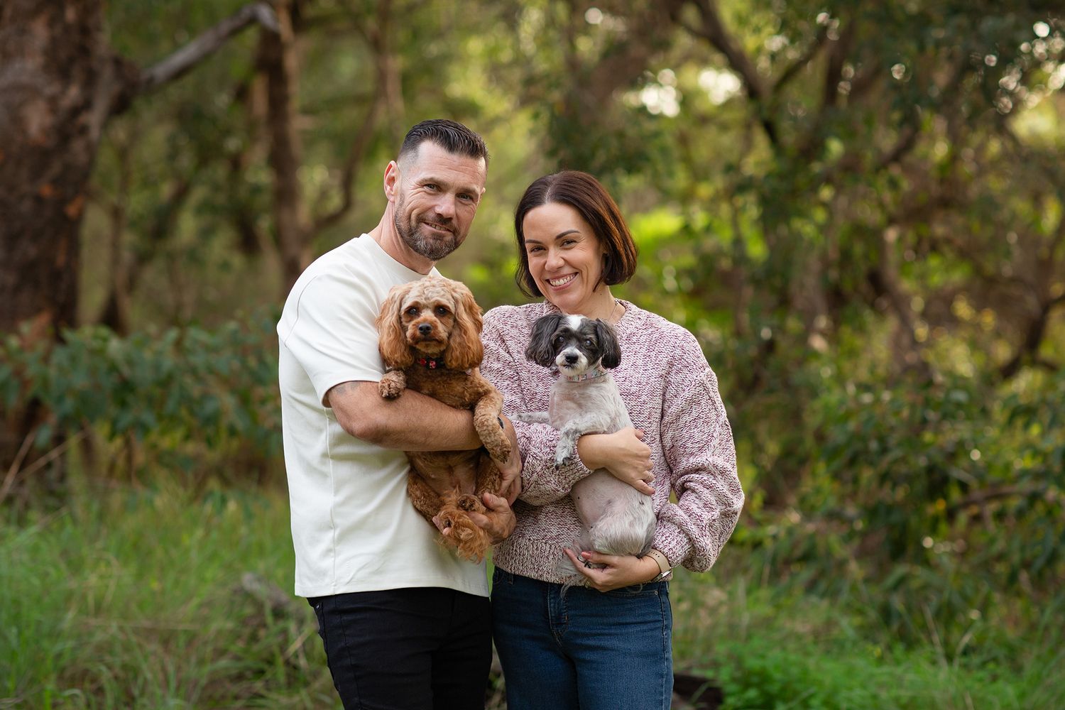 Couple embracing their two dogs at golden hour during a pet photo session in the park in Perth