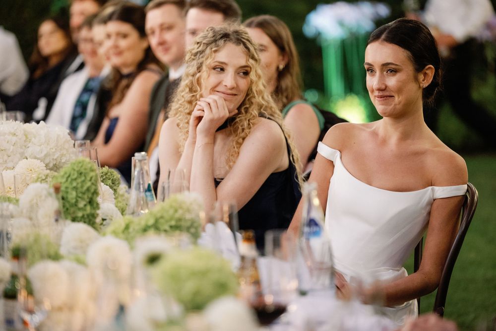 Elegantly dressed wedding guests seated at a beautifully decorated outdoor reception table with white floral arrangements.