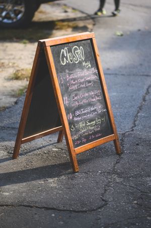 Wooden A-frame chalkboard menu sign on pavement displaying daily specials with colorful chalk writing.