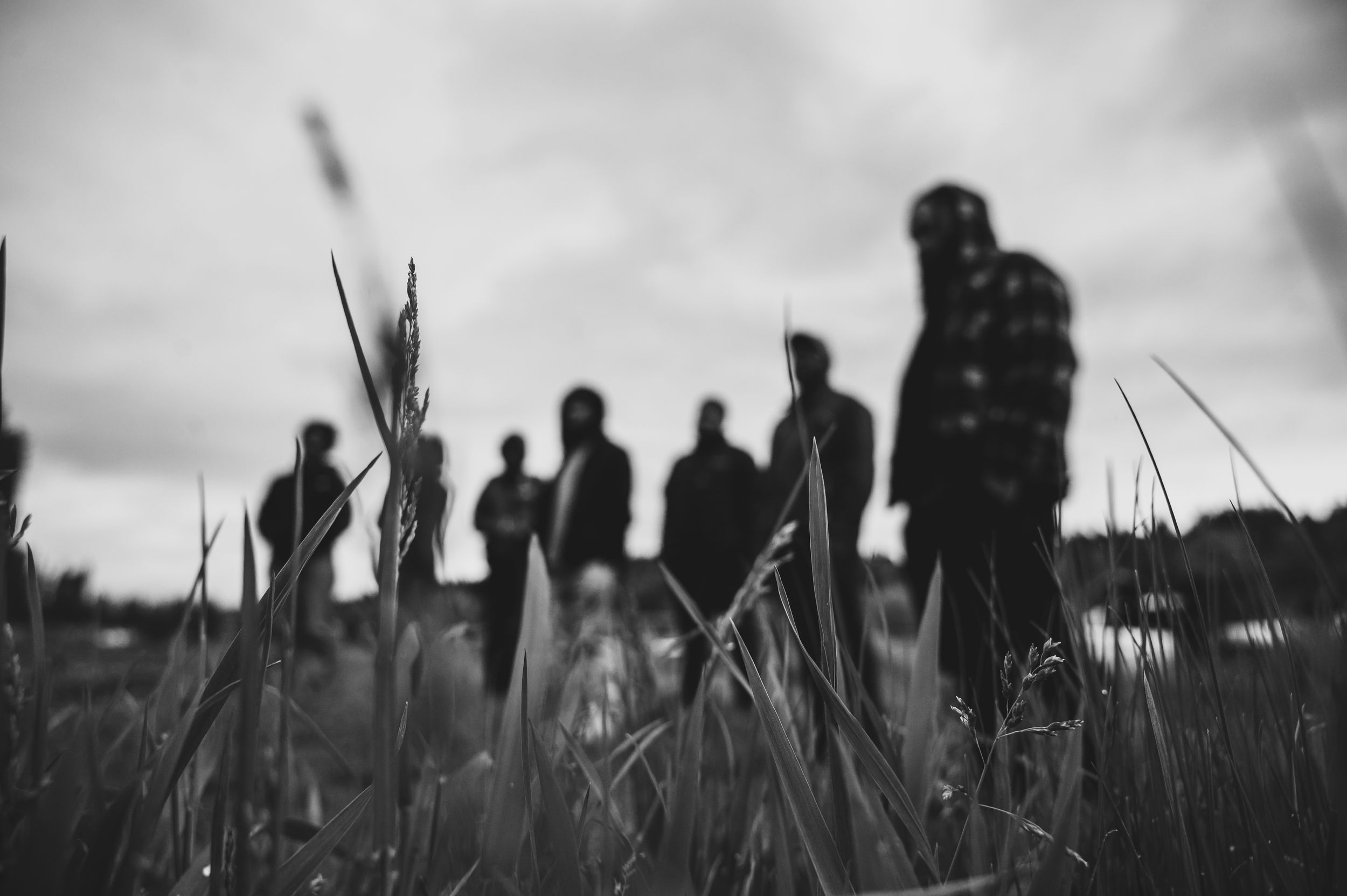Black and white photo of silhouetted group of people standing in a grassy field under overcast skies.