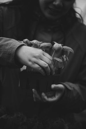 Black and white photo of a smiling woman holding small mushrooms in her hands outdoors.