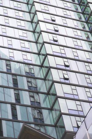 Close-up view of a modern glass skyscraper facade with reflective teal-tinted windows arranged in geometric patterns.