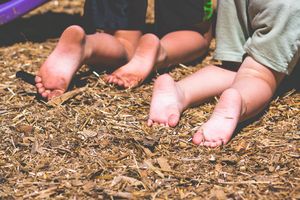 Barefoot children sitting on dry straw ground outdoors, showing their bare feet in a natural setting.