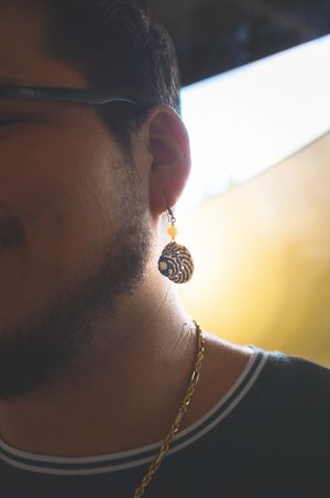Man with glasses and beard wearing a decorative blue and gold drop earring and gold chain necklace.