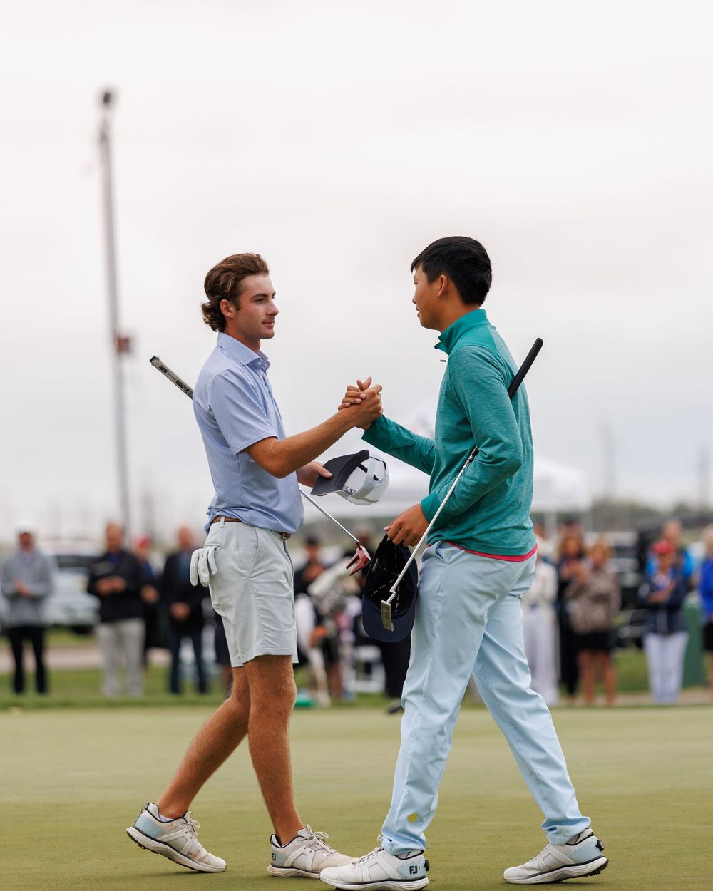 Two young golfers shaking hands on the 18th green after a competitive round.