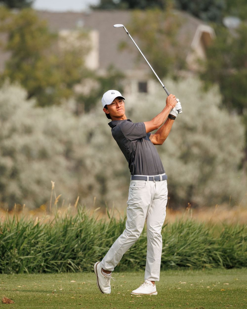 Golfer in white cap follows through on iron shot on the fairway.