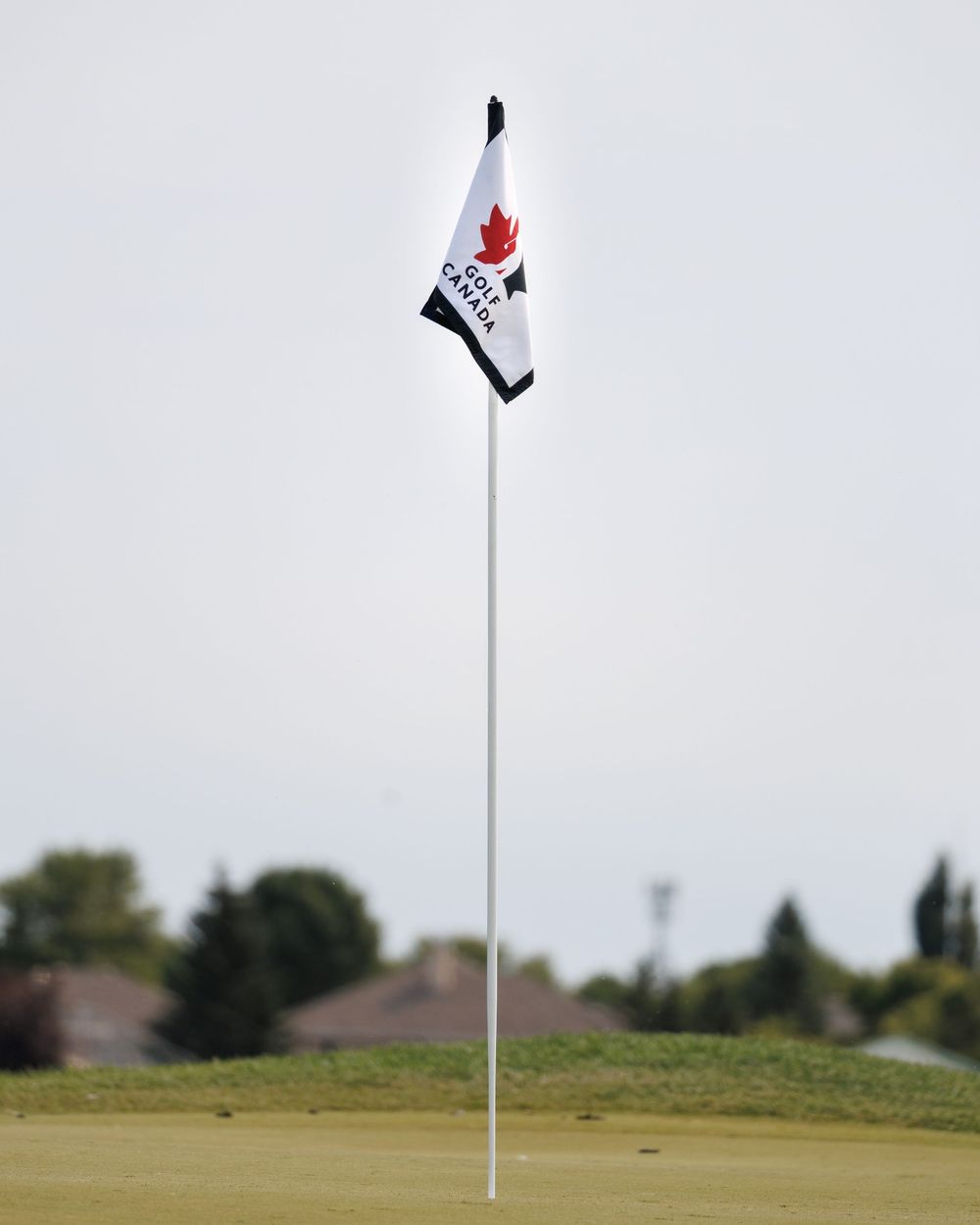 Golf Canada branded pin flag on a golf course hole against cloudy sky.