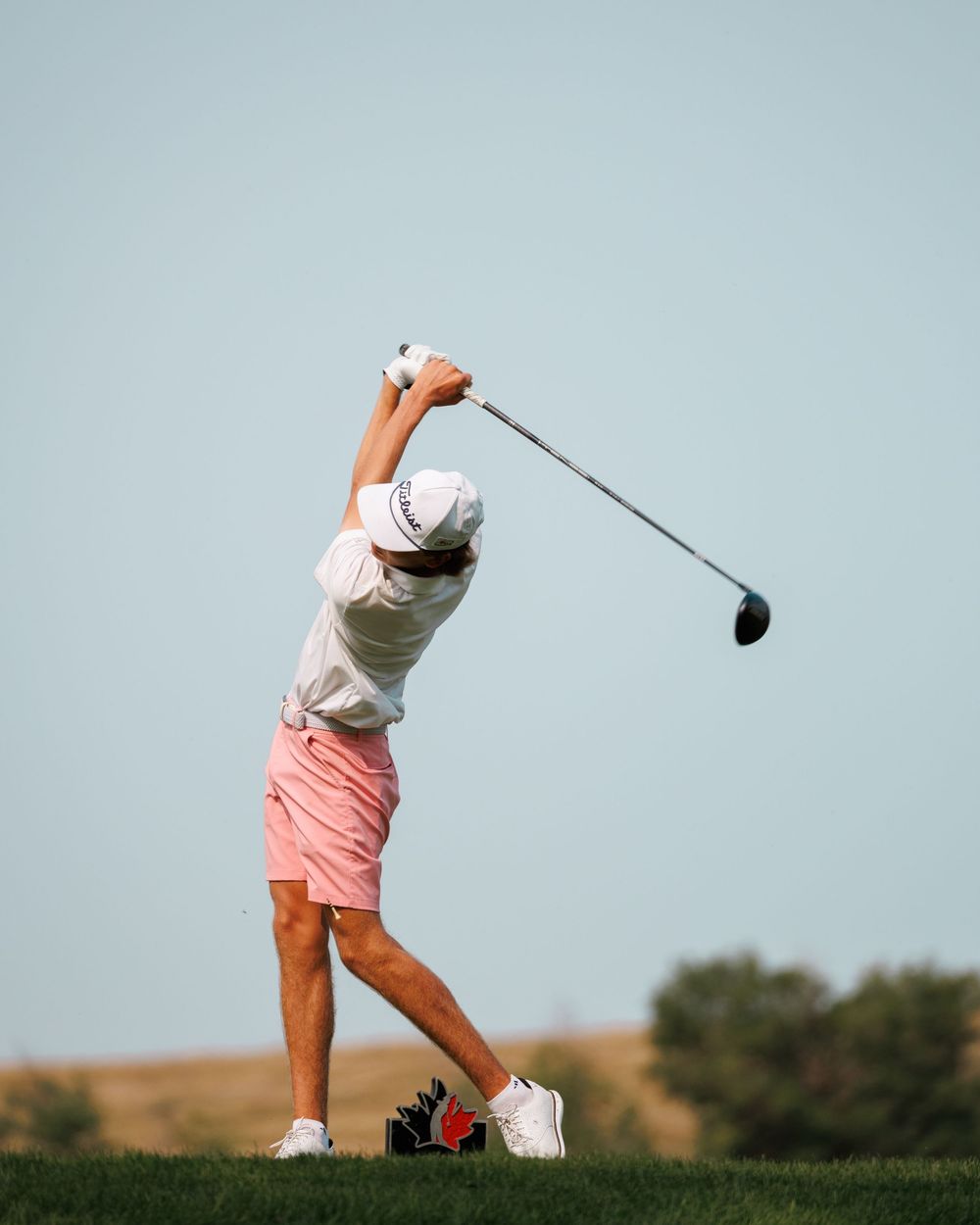 Junior golfer completes full driver swing follow-through in pink shorts.
