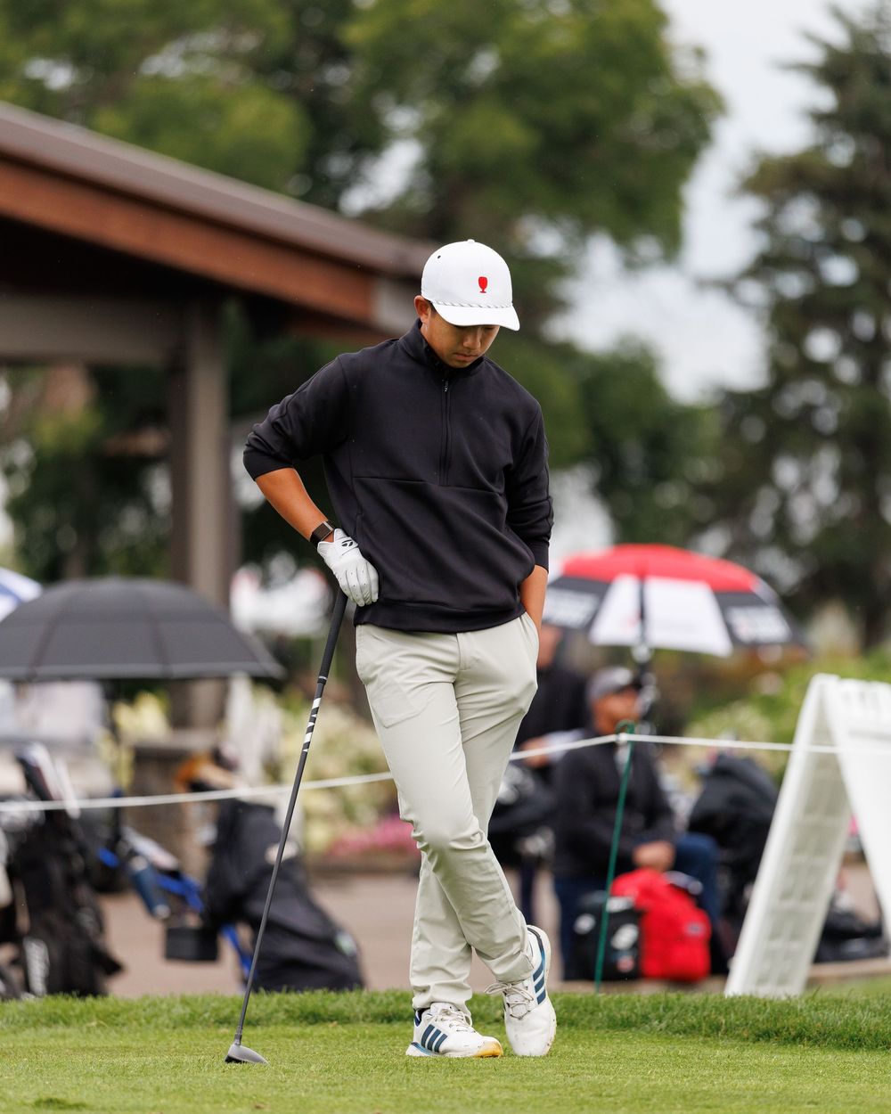 Junior golfer in black sweater and white cap studies his shot on the course.