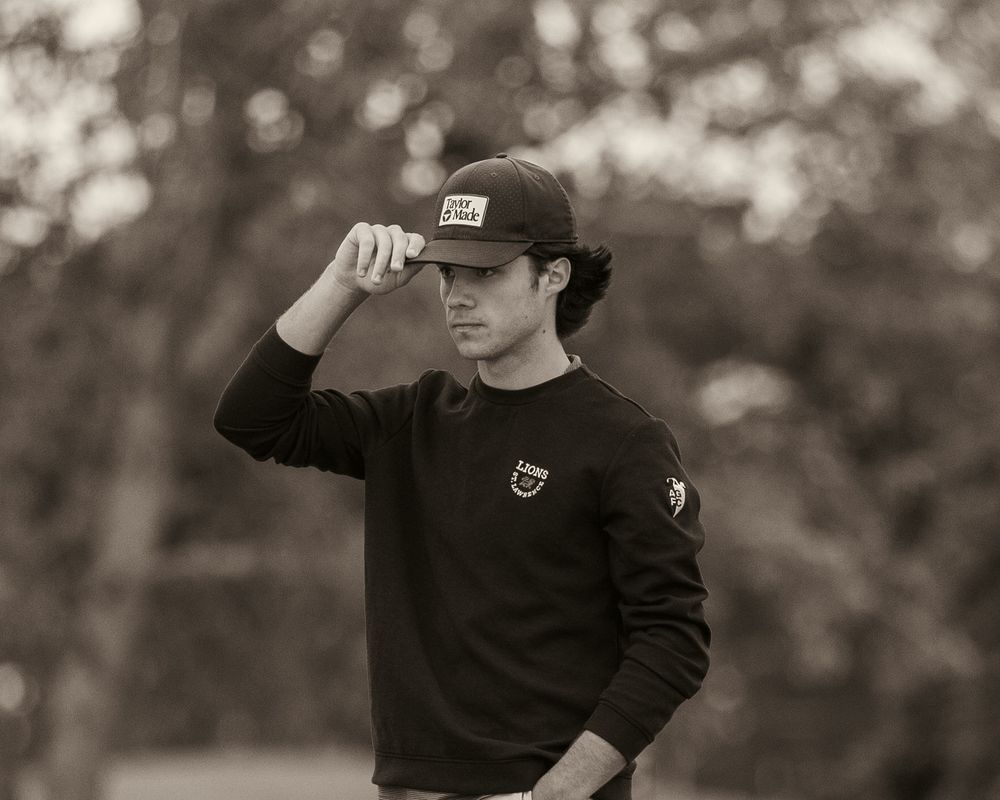 Young golfer adjusting his cap in a stylish black and white portrait photo outdoors.