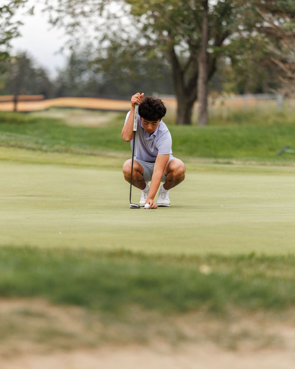 Golfer crouching to line up a putt on a lush green golf course fairway.