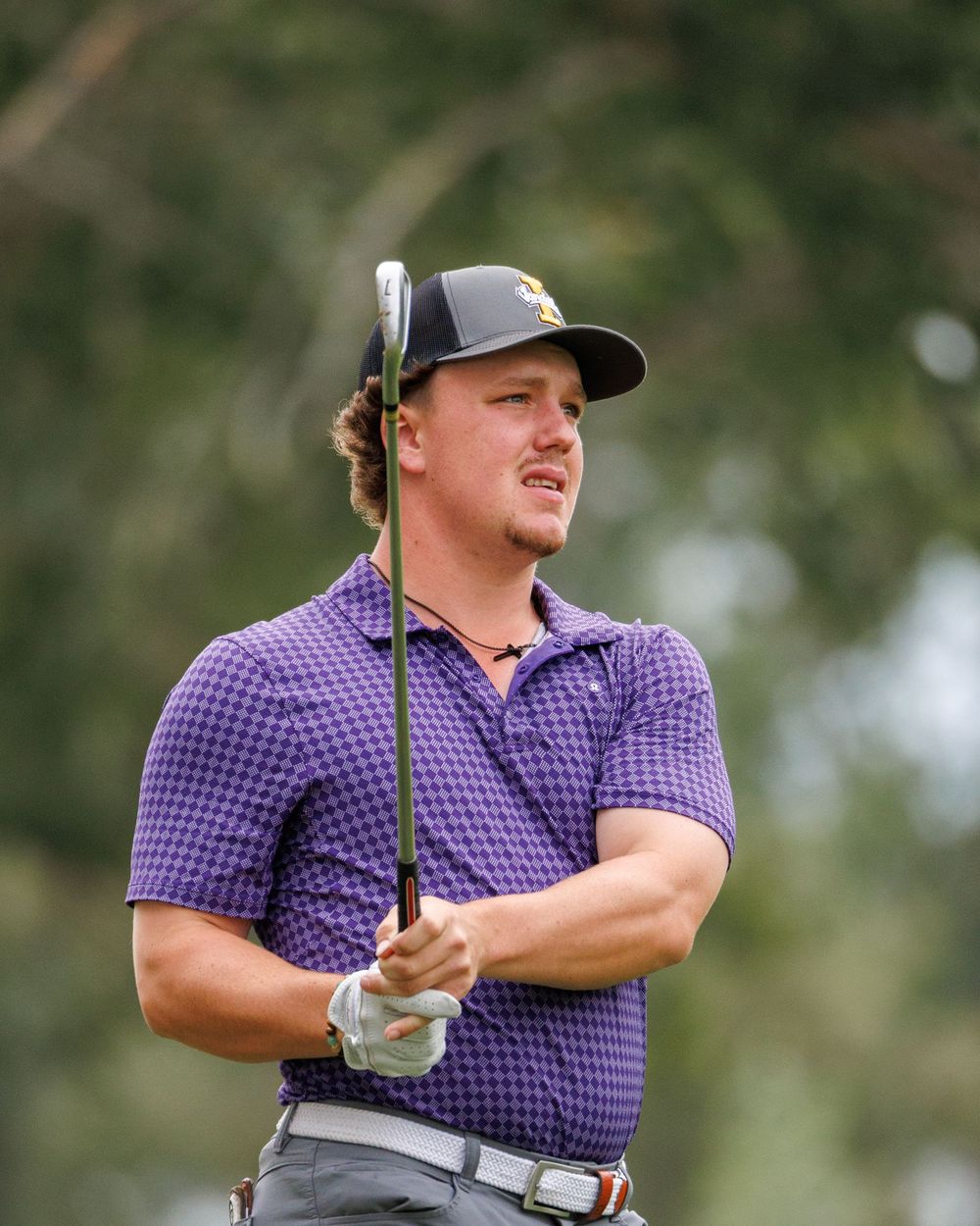 Male golfer in purple polo shirt watching his shot while holding a golf club.