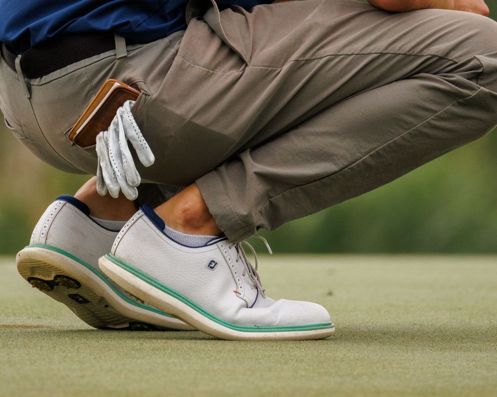 Close-up of golfer wearing FootJoy shoes and glove crouching on a putting green.
