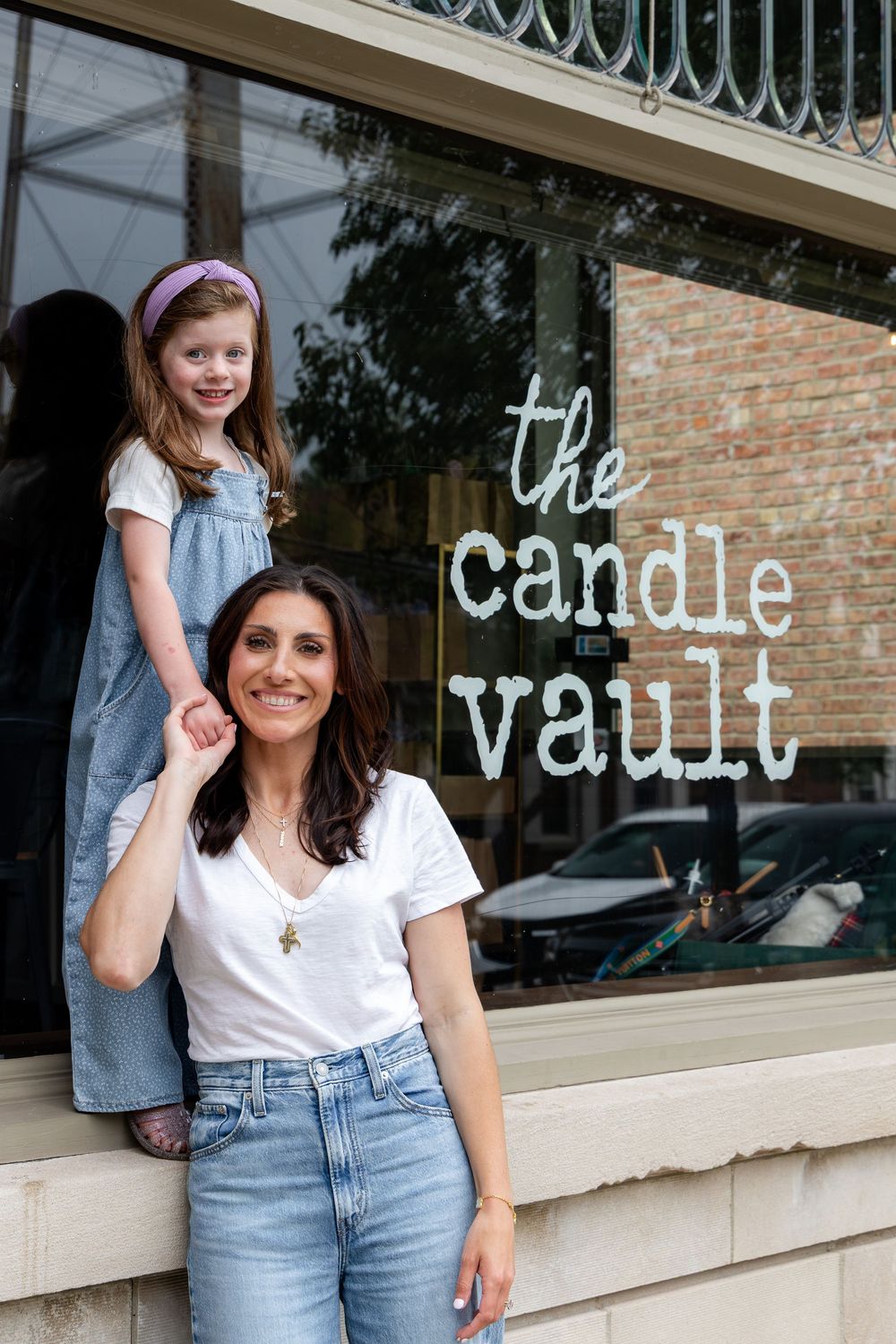 Woman and young girl posing in front of The Candle Vault store, smiling outdoors on a sunny day.