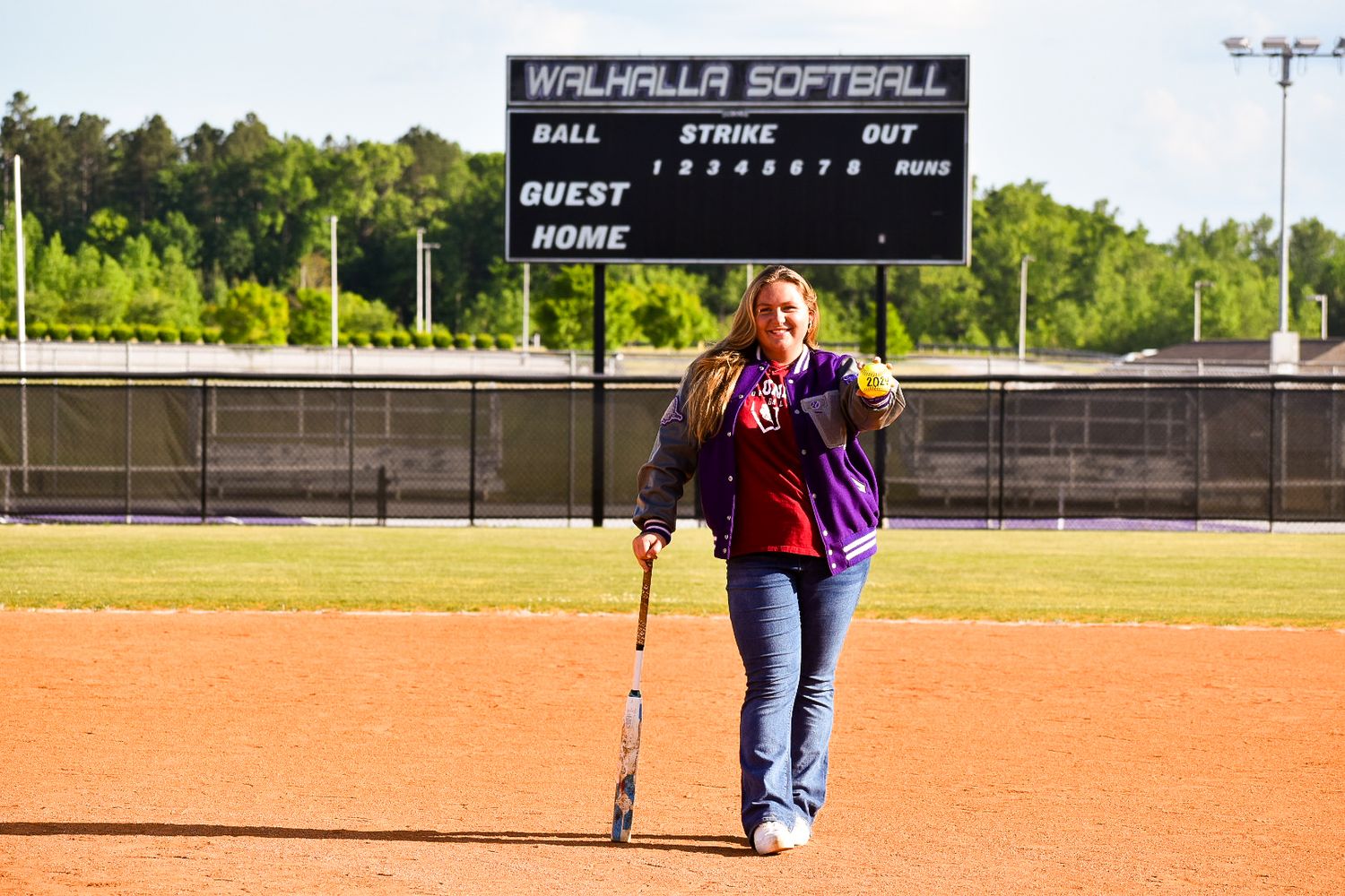 Woman holding softball bat on Walhalla Softball field with scoreboard in background.