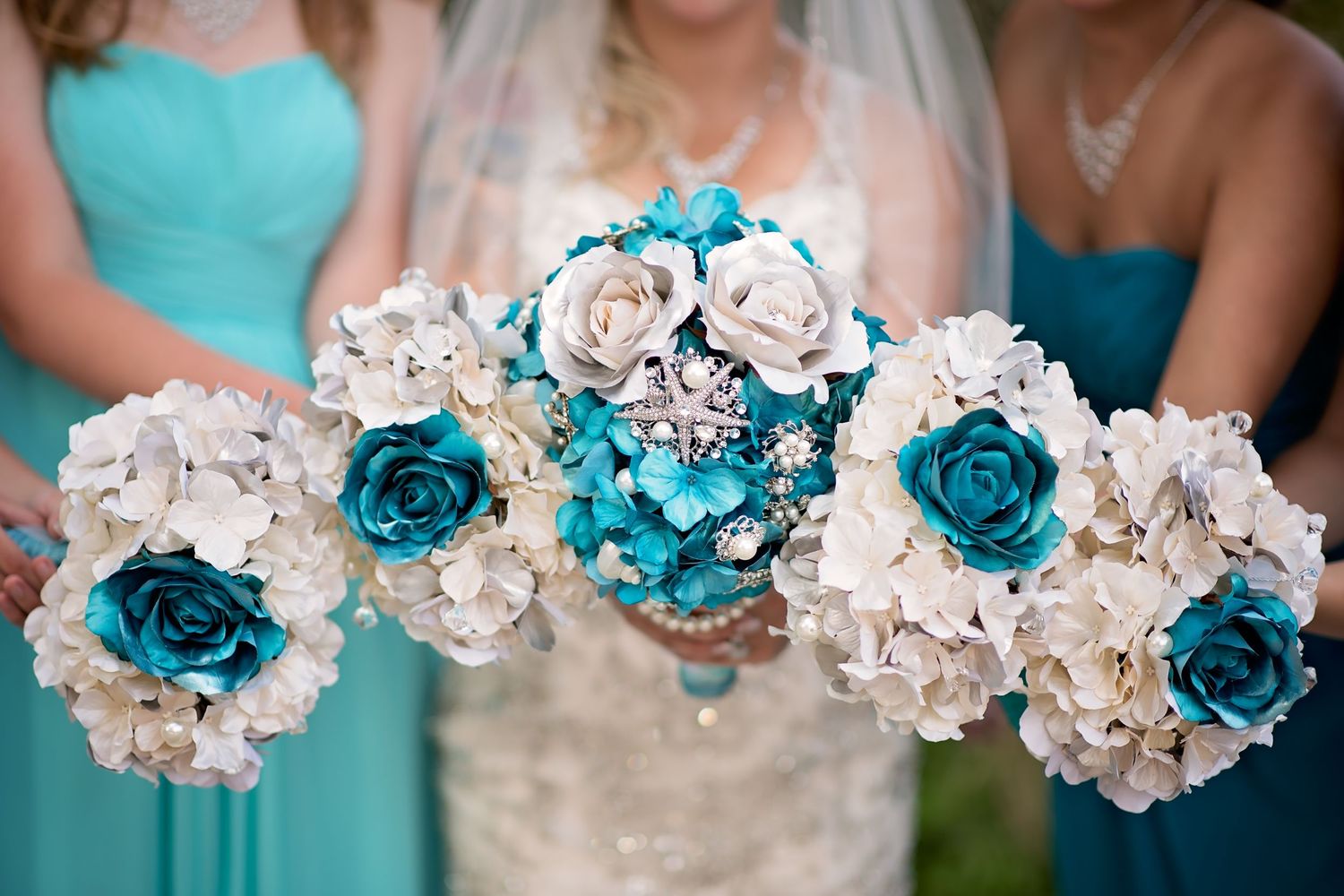 Bride and bridesmaids holding teal and white floral bouquets at wedding.
