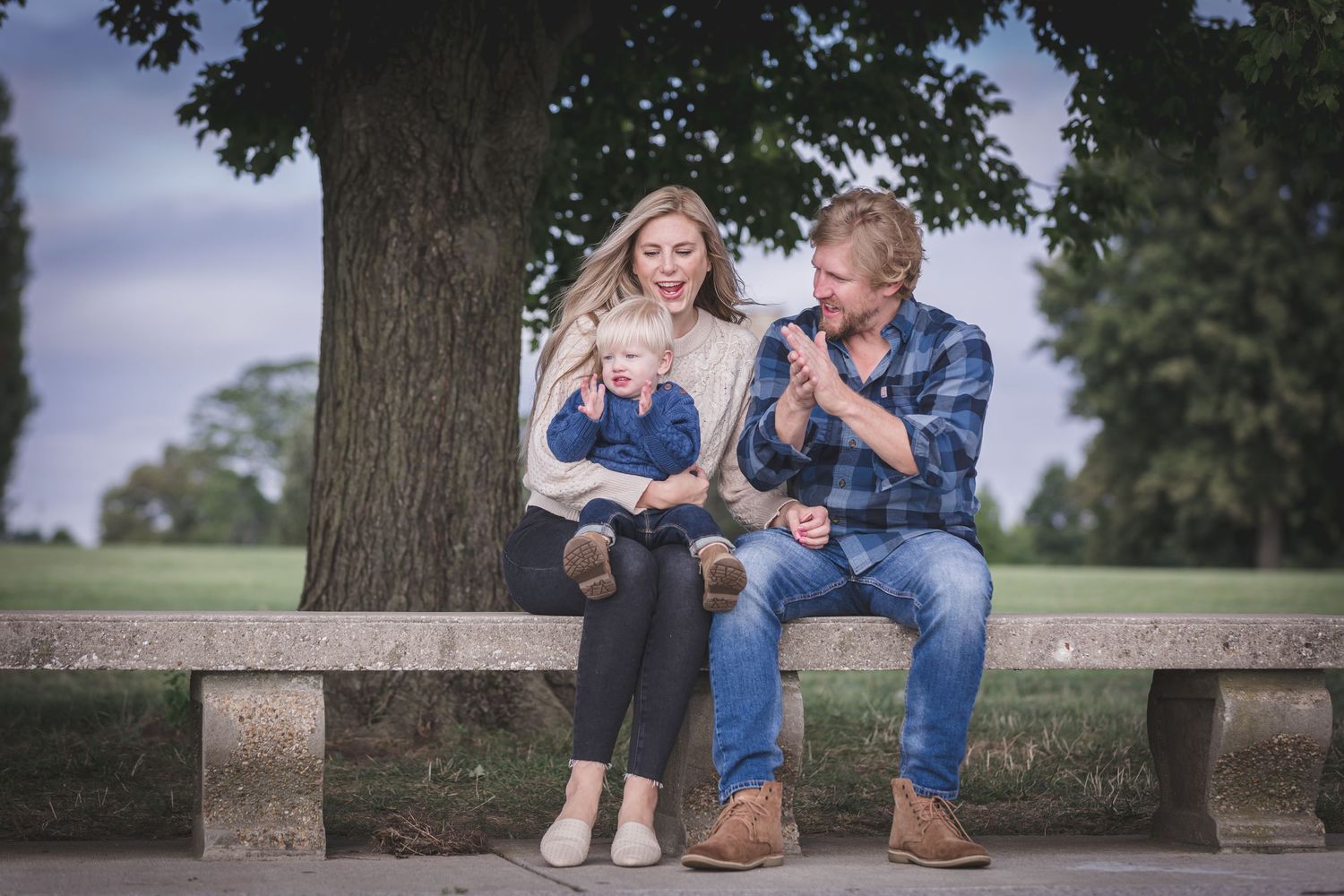 Family of three posing together outdoors in a park.