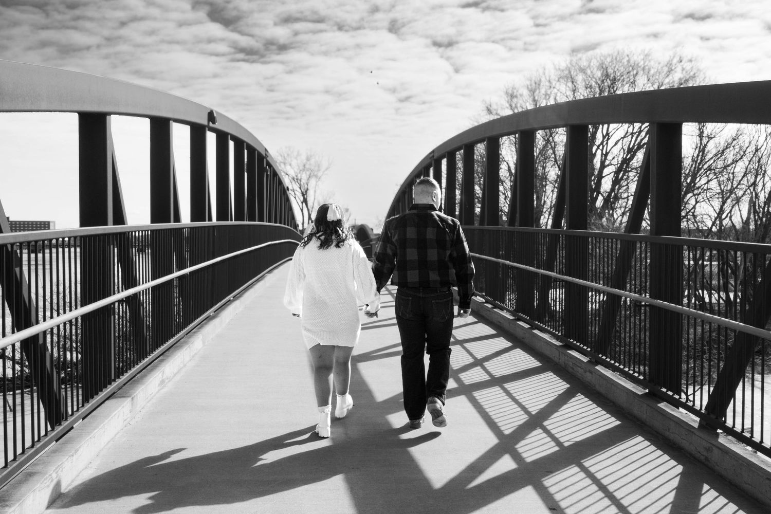 An engaged couple walks hand in hand across a bridge during a romantic engagement session.