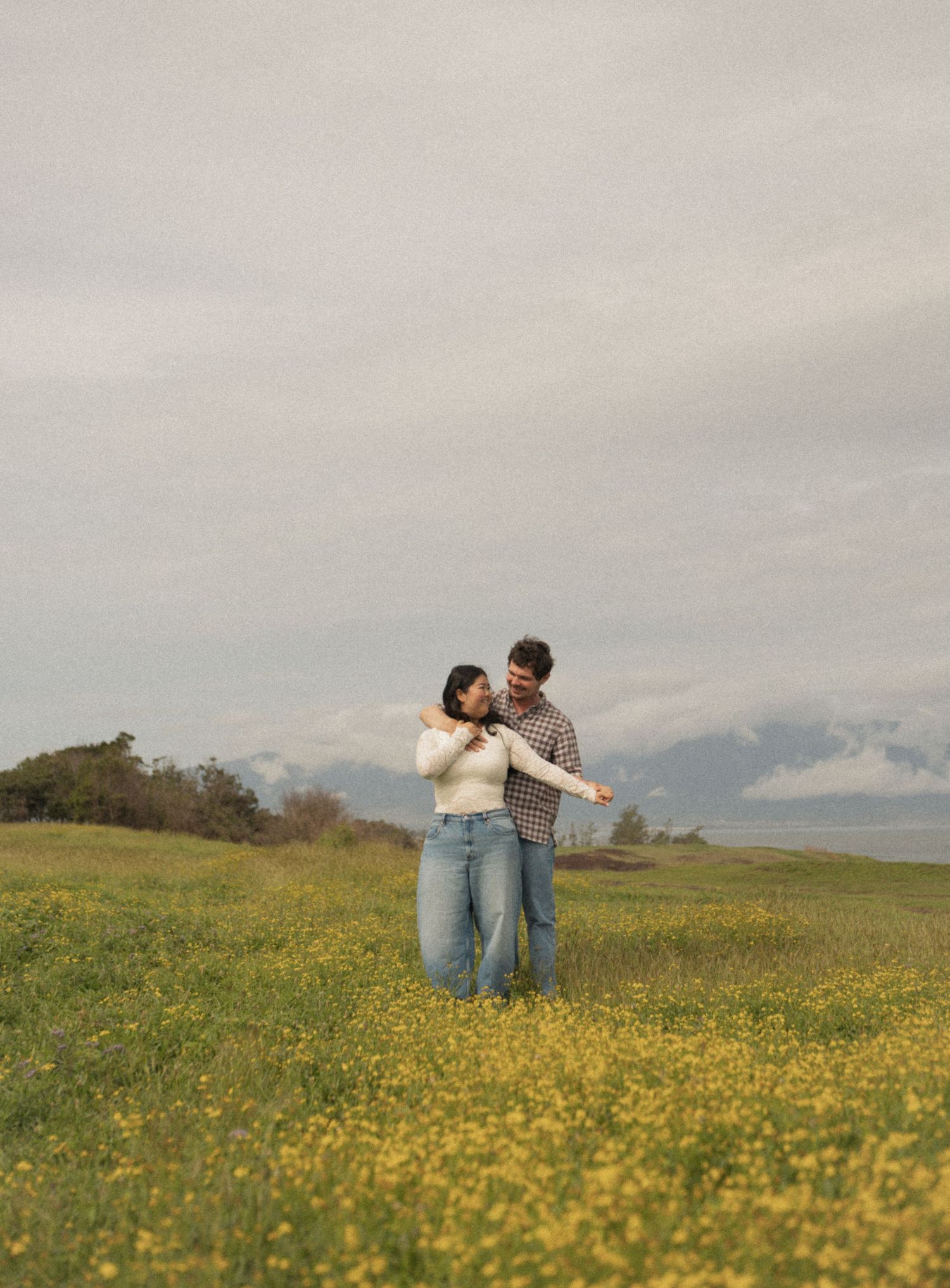 Two people walking along a grassy coastal cliff under a dramatic cloudy sky with ocean views.