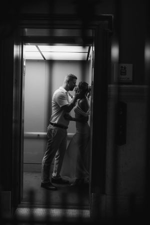 Dramatic black and white silhouette of a couple embracing intimately inside an elevator doorway.