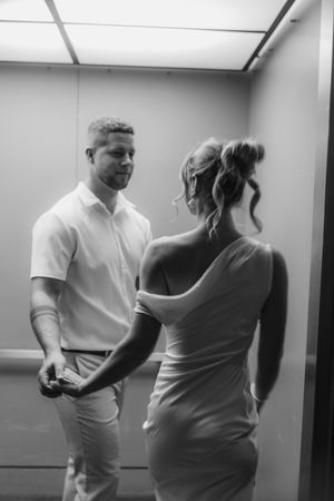 Black and white photo of a couple holding hands and sharing an intimate moment inside an elevator.