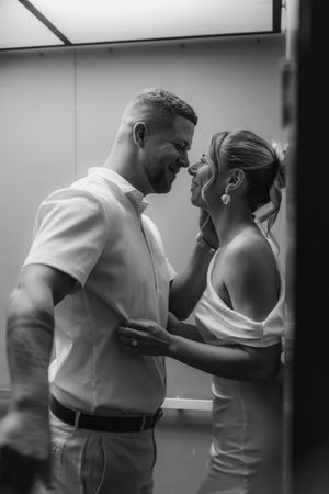 Black and white romantic photo of a smiling couple about to kiss inside a bright elevator.