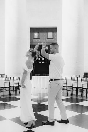 Black and white photo of newlyweds sharing first dance on checkered floor in elegant wedding venue.