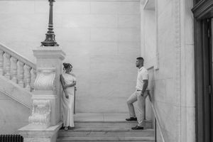 Black and white photo of bride and groom standing apart on marble steps of historic building.
