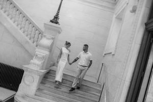 Aerial black and white view of bride and groom holding hands on elegant marble staircase.