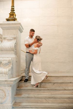 Groom tenderly holds brides face on marble staircase in elegant courthouse wedding venue.