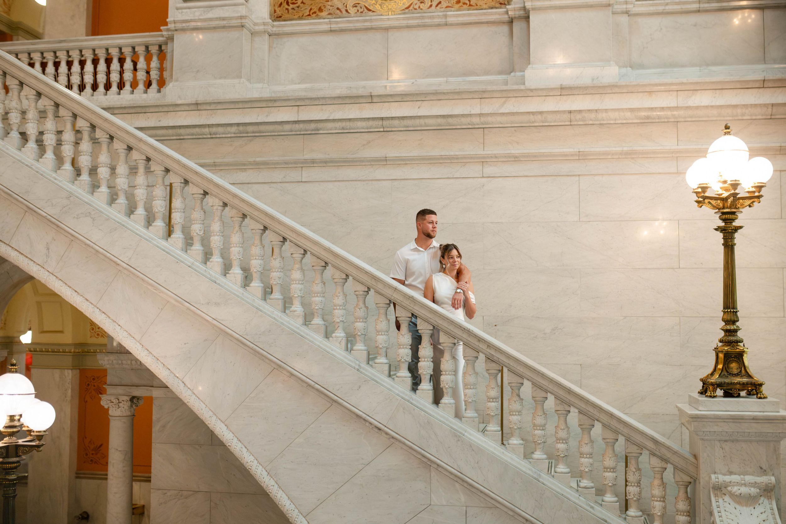 Bride and groom stand together on sweeping marble staircase in elegant courthouse venue.