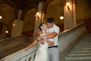Bride and groom share a romantic kiss on grand marble staircase with ornate columns.