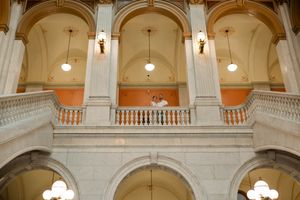 Bride and groom pose on upper balcony of grand marble courthouse wedding venue.