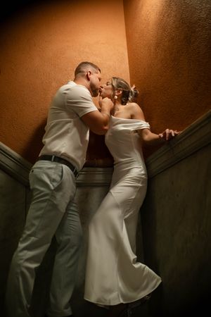 Bride and groom sharing a passionate kiss against a warm-toned wall in a dimly lit corner.