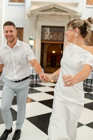 Laughing newlyweds holding hands and running across a classic black and white checkered dance floor.