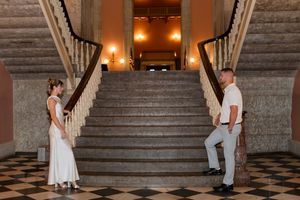 Bride and groom standing apart on a grand marble staircase in an elegant historic building.